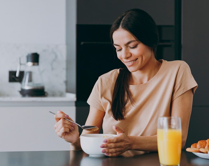 Mujer sonriendo y desayunando en su cocina